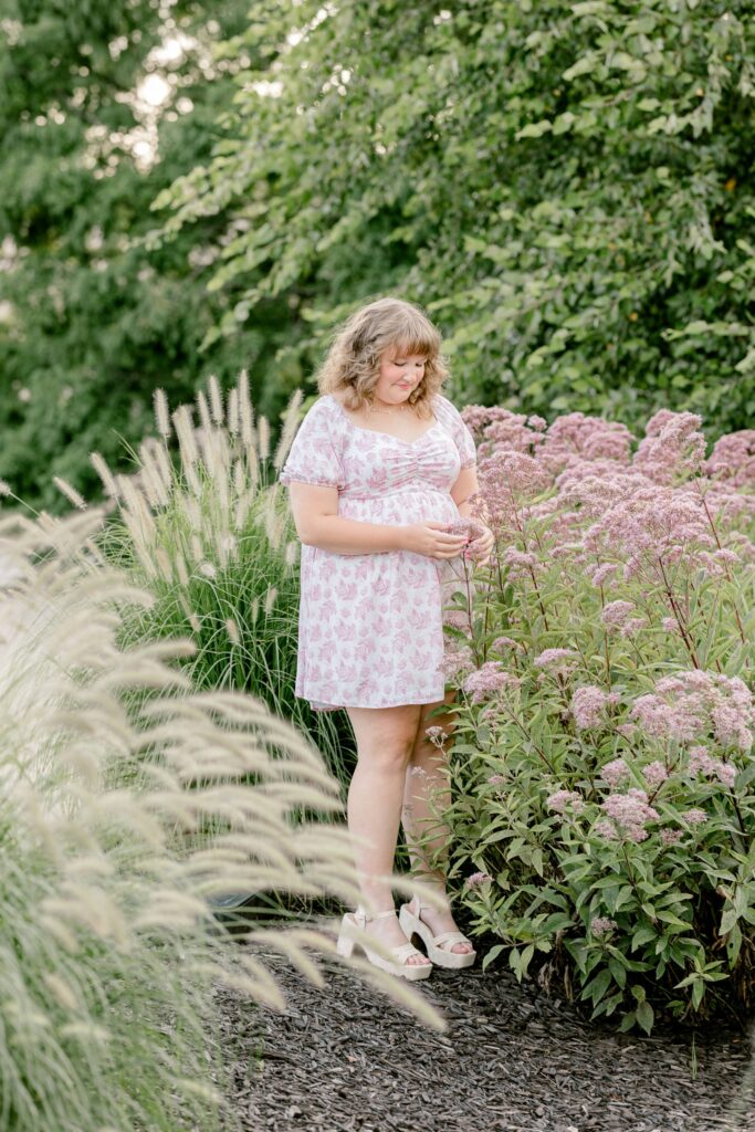 Senior girl in a floral dress among tall grasses and purple flowers in a Grand Rapids garden
