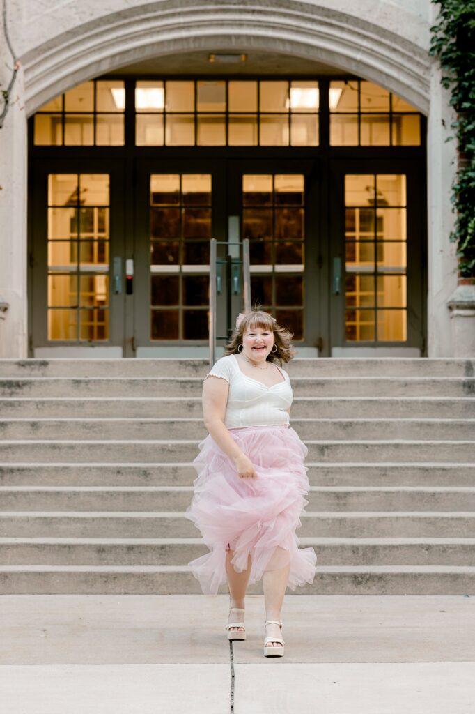 Senior girl in a pink tulle skirt on the steps of a historic ivy-covered building in Grand Rapids