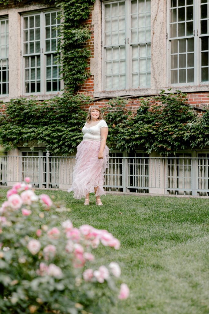 Senior portrait with pink roses in front of an ivy-covered building in Grand Rapids