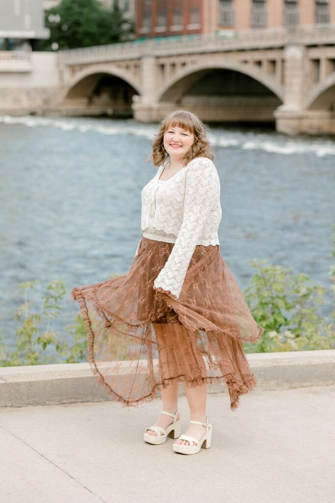 Senior portrait by the Grand River with an arched bridge in Grand Rapids