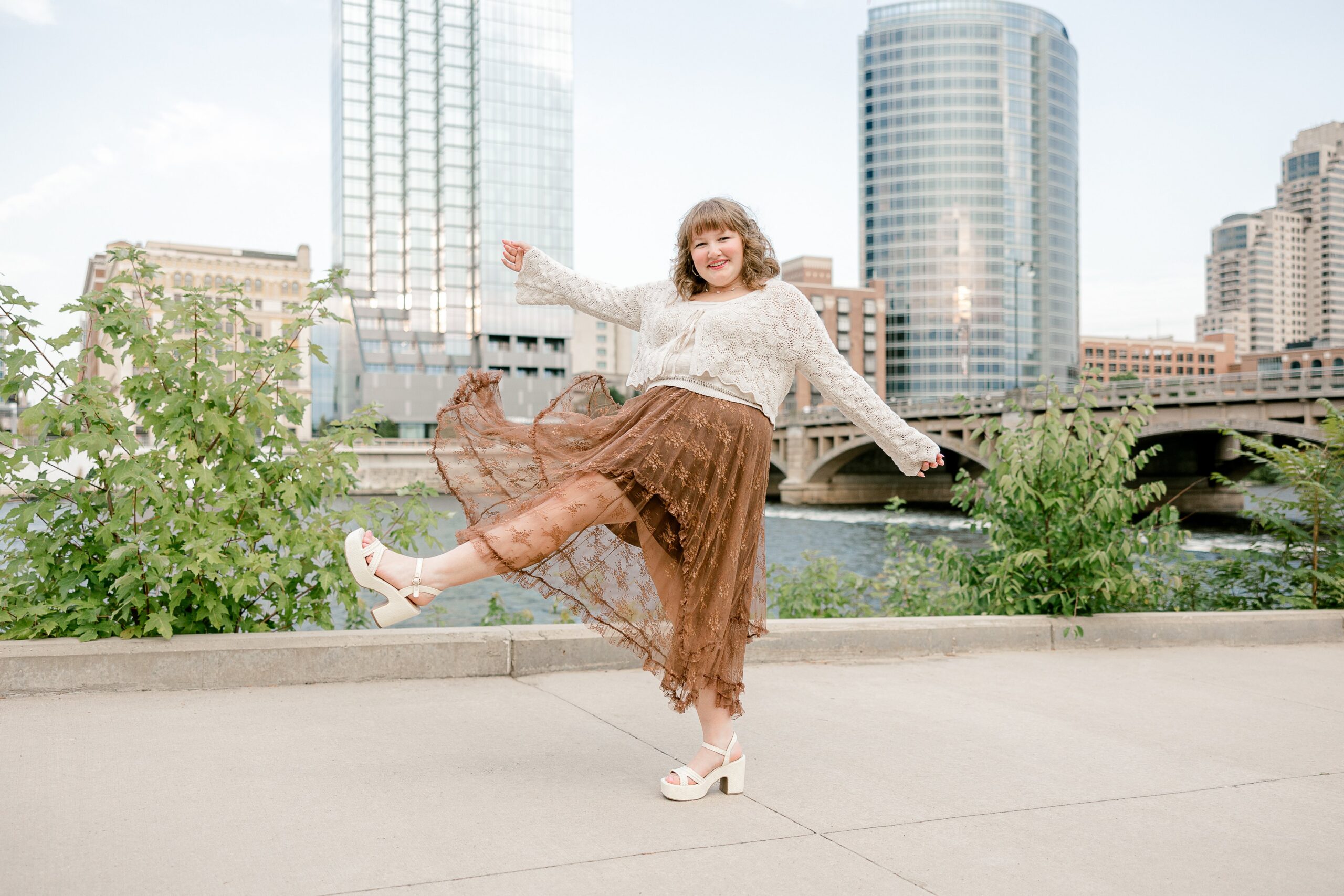 Senior girl twirling along the Grand River with the downtown Grand Rapids skyline behind her