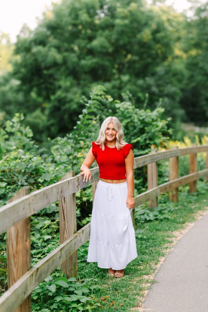 Senior girl leaning on a wooden fence along a trail at Grand Ravines