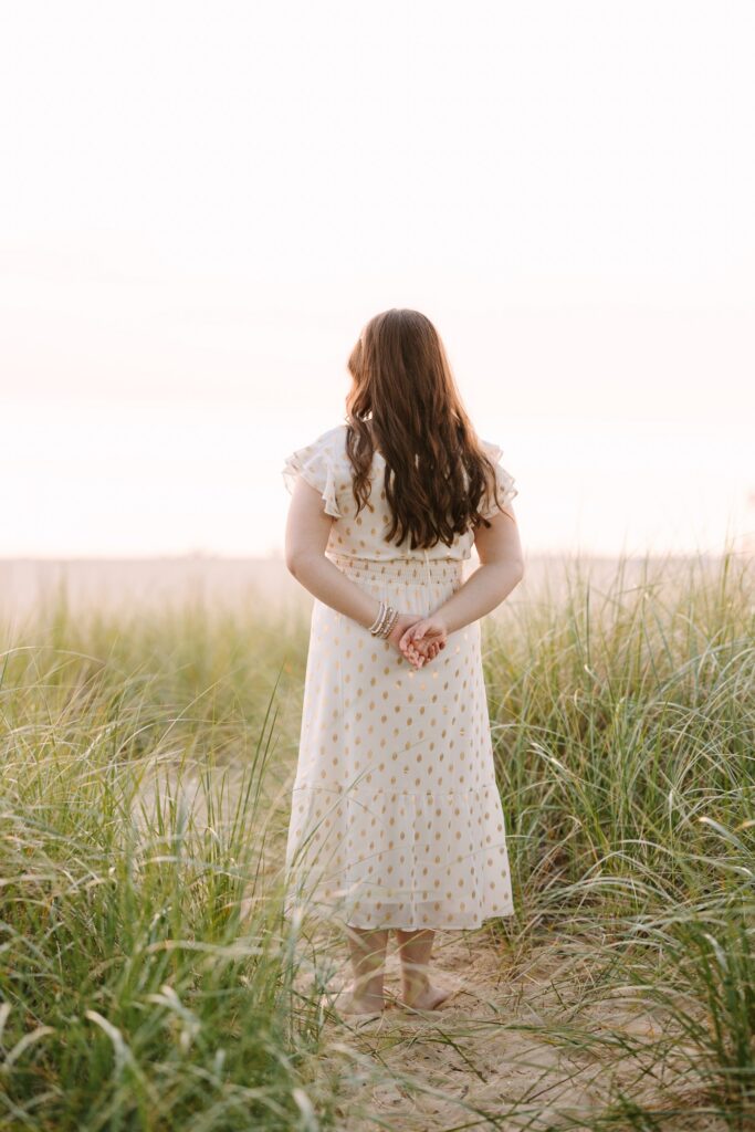 Senior girl in a white dress standing in dune grass near Lake Michigan
