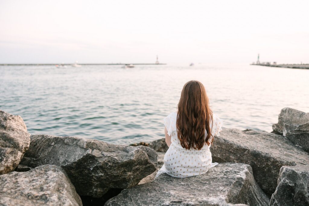 Senior girl sitting on the rocks at sunset on Lake Michigan at Holland State Park