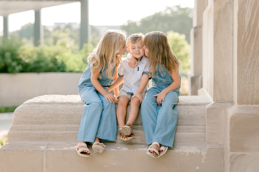 Sisters kissing their little brother on the cheek on a stone ledge in downtown Grand Rapids
