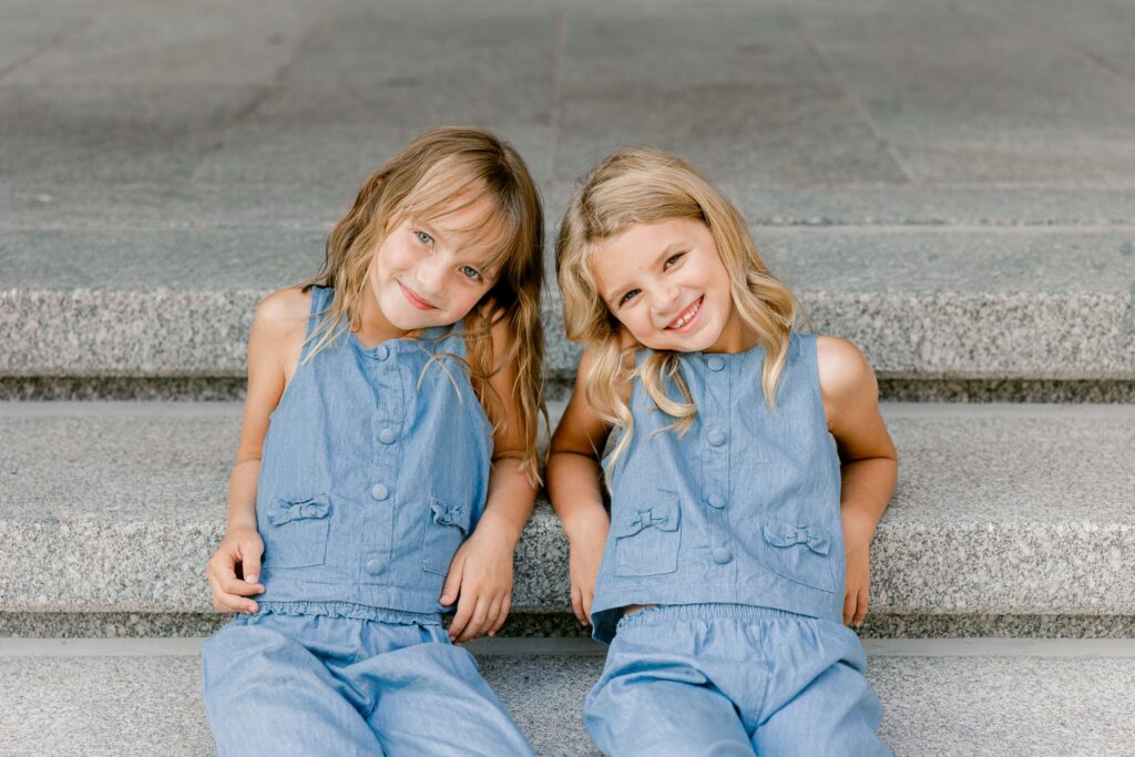 Two sisters in matching denim leaning their heads together on the steps at DeVos Place