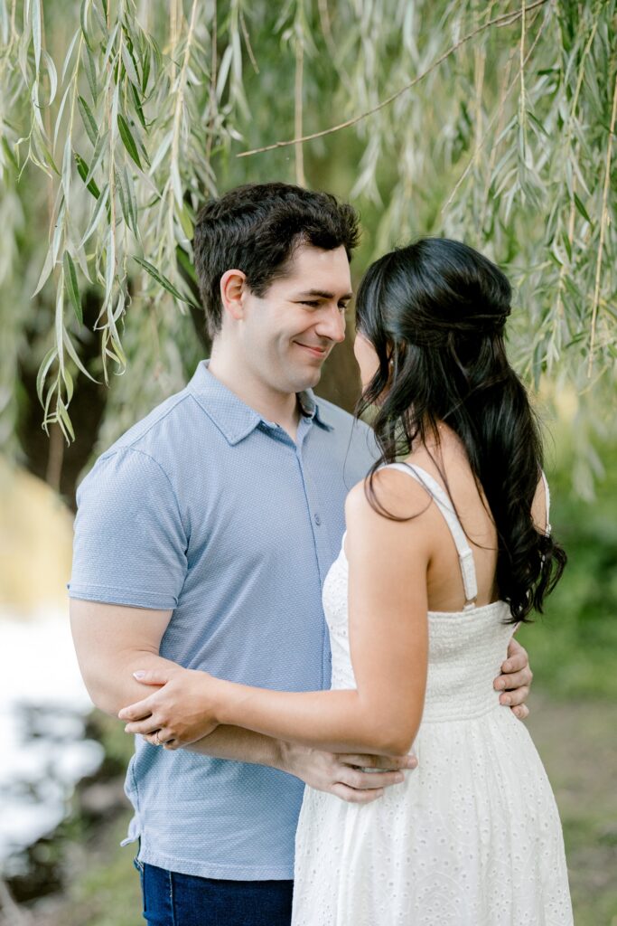 Couple holding each other close under the willows during a summer engagement session in Grand Rapids