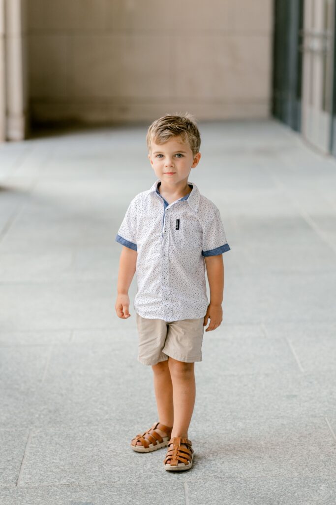 Young boy in a button-up shirt and shorts standing in the colonnade at DeVos Place