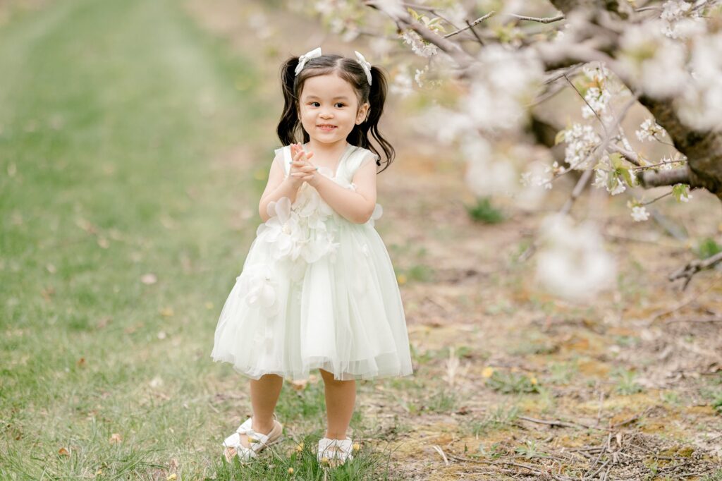 Toddler framed by blooming apple blossom branches in the orchard at Robinette's Apple Haus