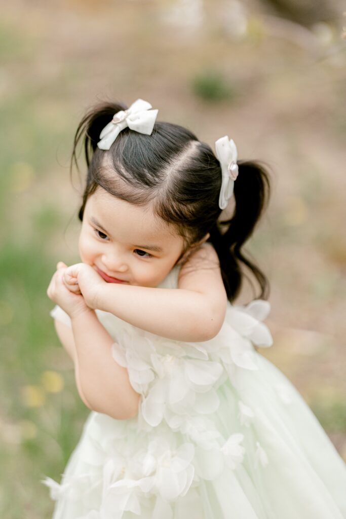 Close-up of a smiling toddler in a white tulle dress with pigtail bows in the apple orchard