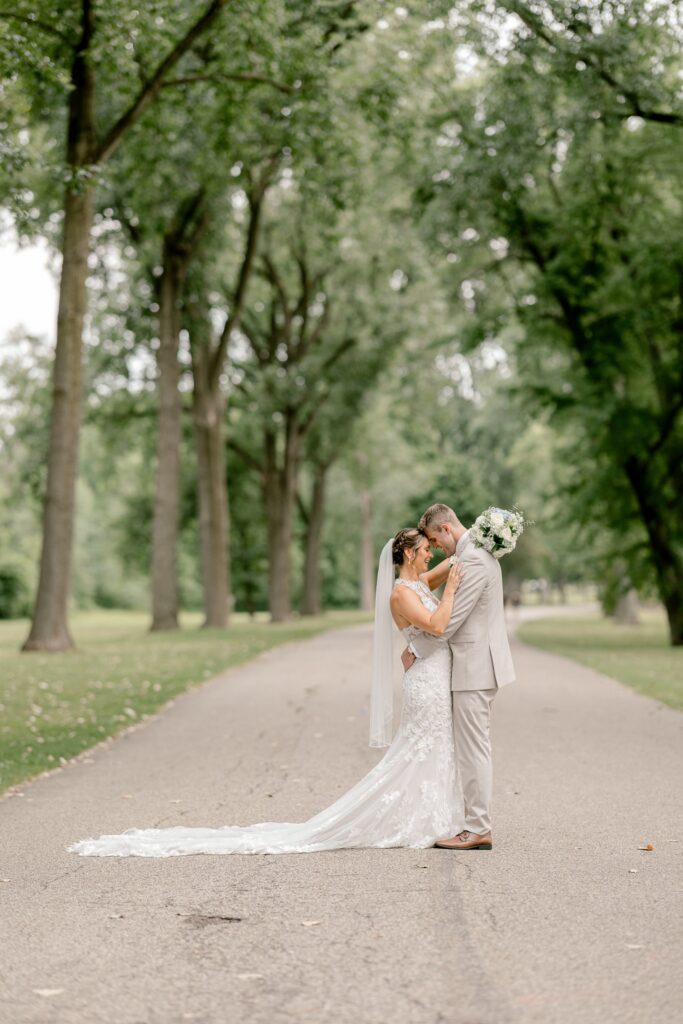 Bride and groom walking down a tree-lined path in Grand Rapids