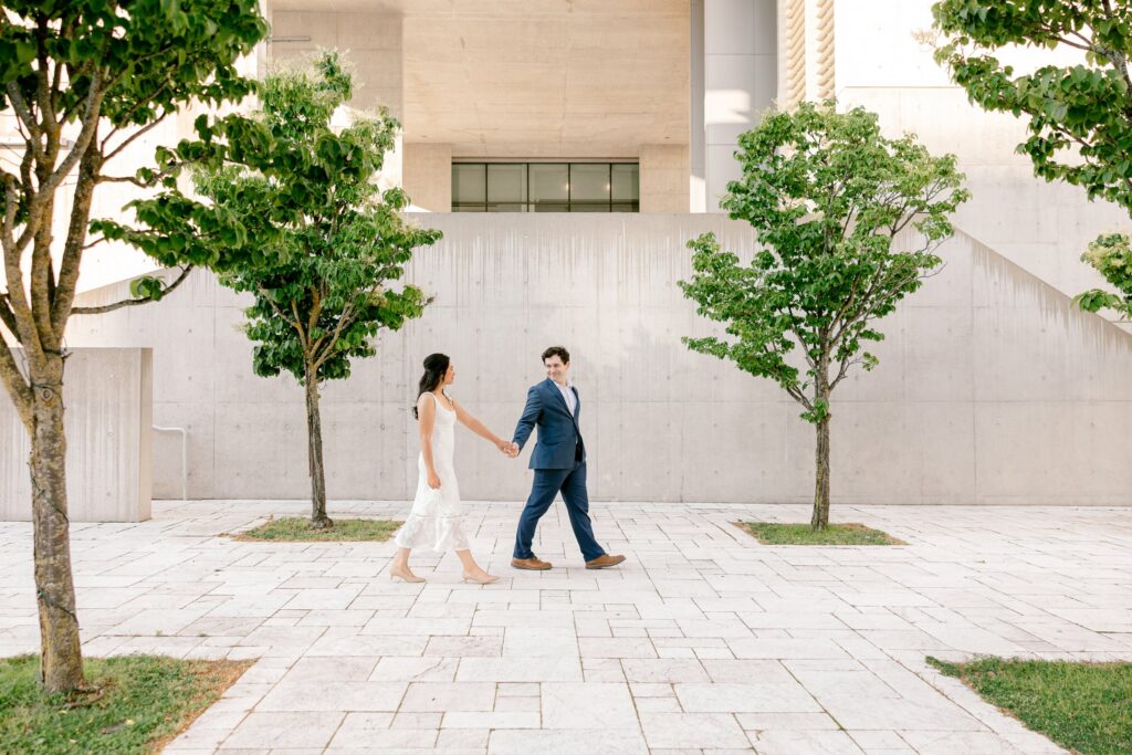 Couple walking hand in hand past young trees on a downtown Grand Rapids plaza