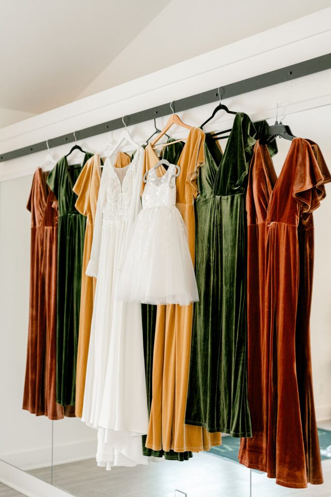 Rust, mustard and green velvet bridesmaid dresses hanging beside the wedding dress