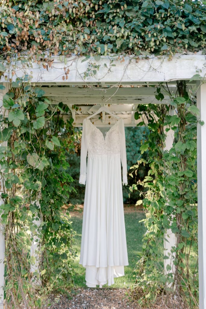 Wedding dress hanging under an ivy covered pergola at Ivy House