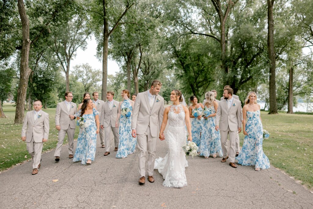 Wedding party in blue floral dresses and tan suits on a tree-lined path in Grand Rapids
