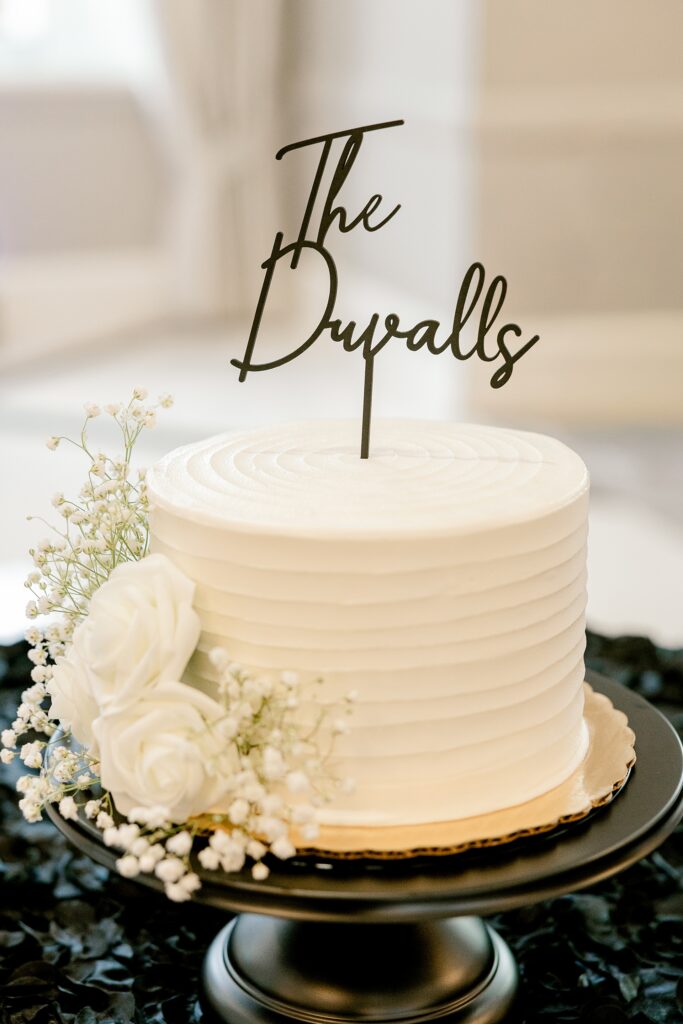 White wedding cake with a script cake topper on a black stand